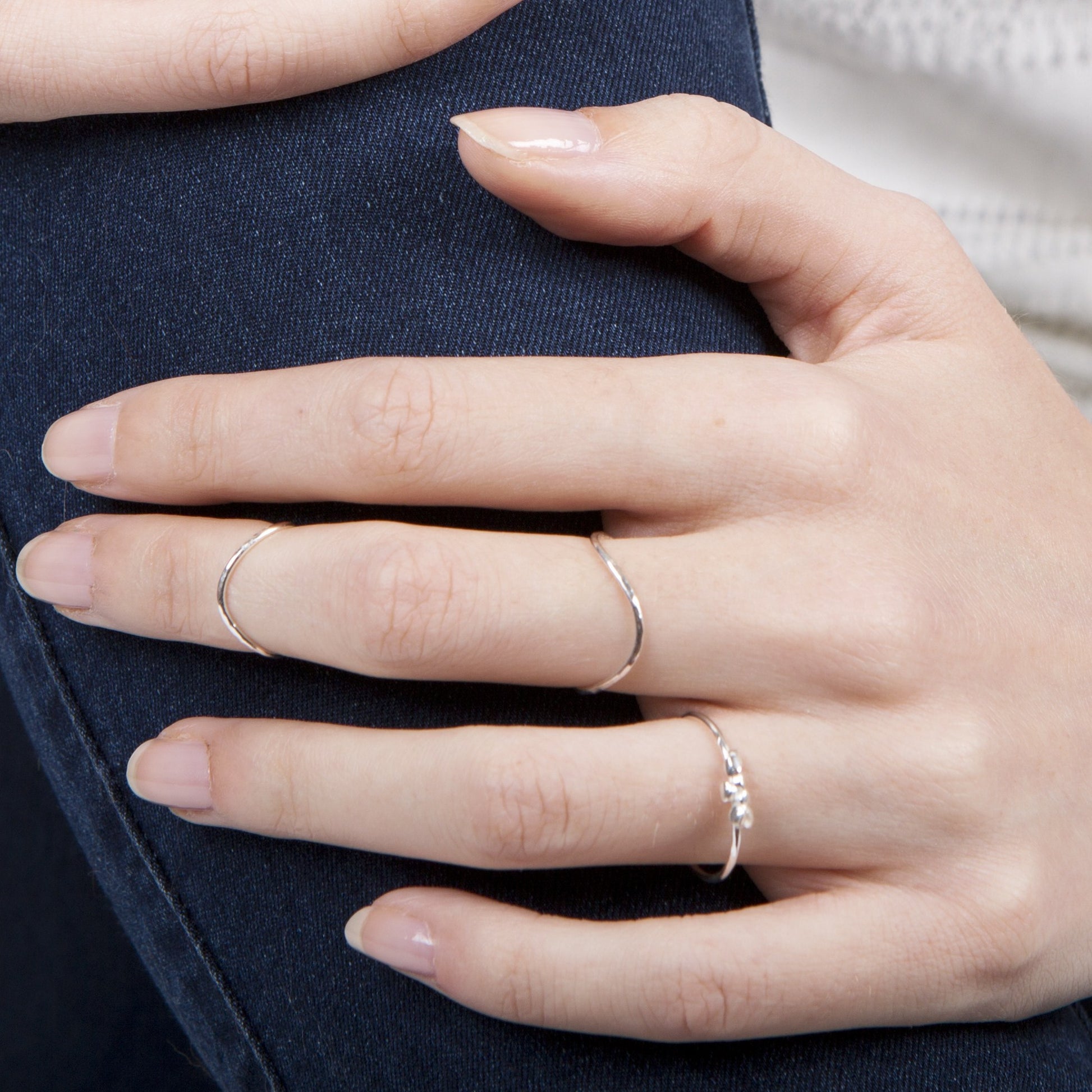 A person's hand displaying a slim sterling silver midi ring with a hammered texture on the finger.