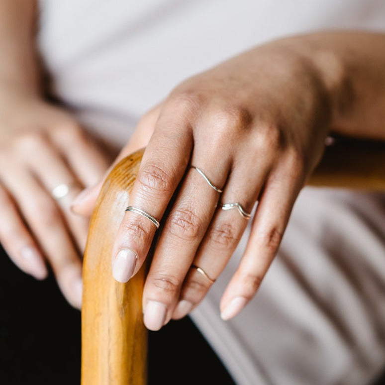 A hand with a selection of thin rings in sterling silver and 9ct gold, leaning on a chair arm