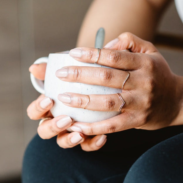 A hand wearing a selection of thin rings, holding a mug