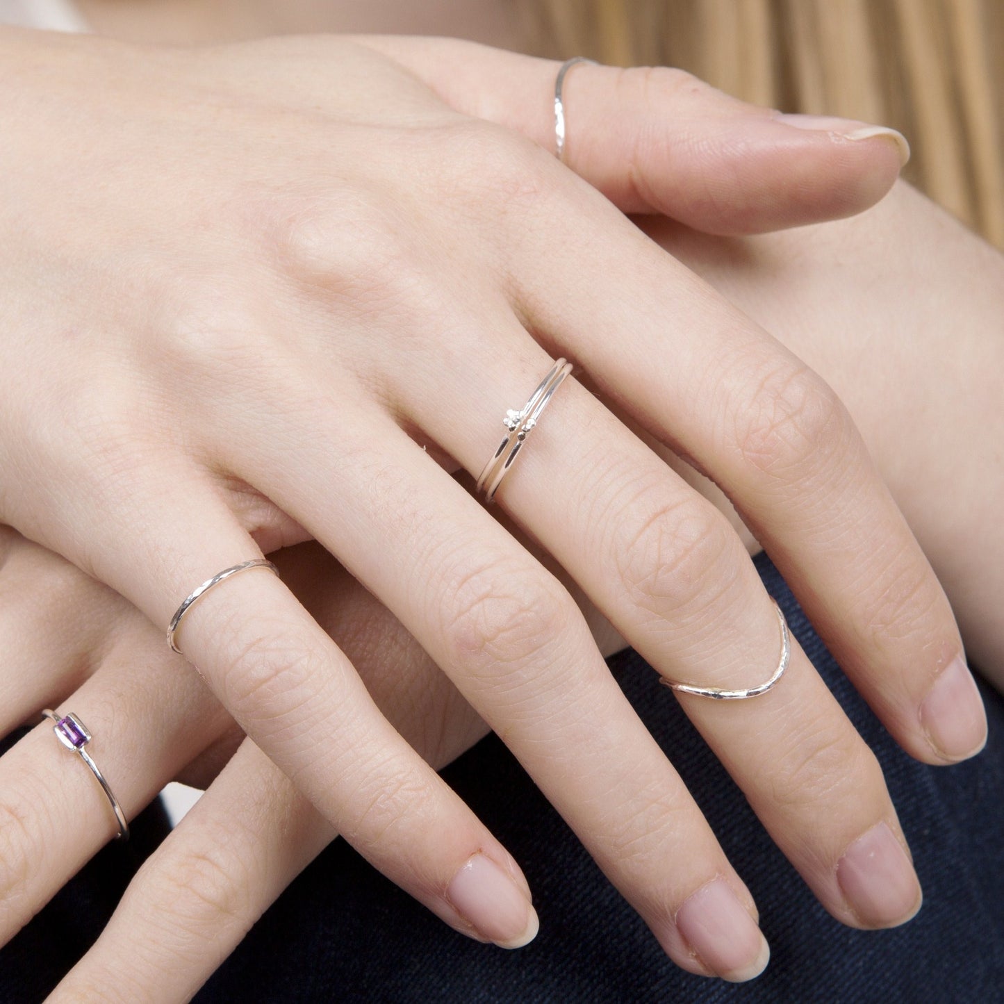 A selection of thin silver rings being worn, hands overlapped on a knee