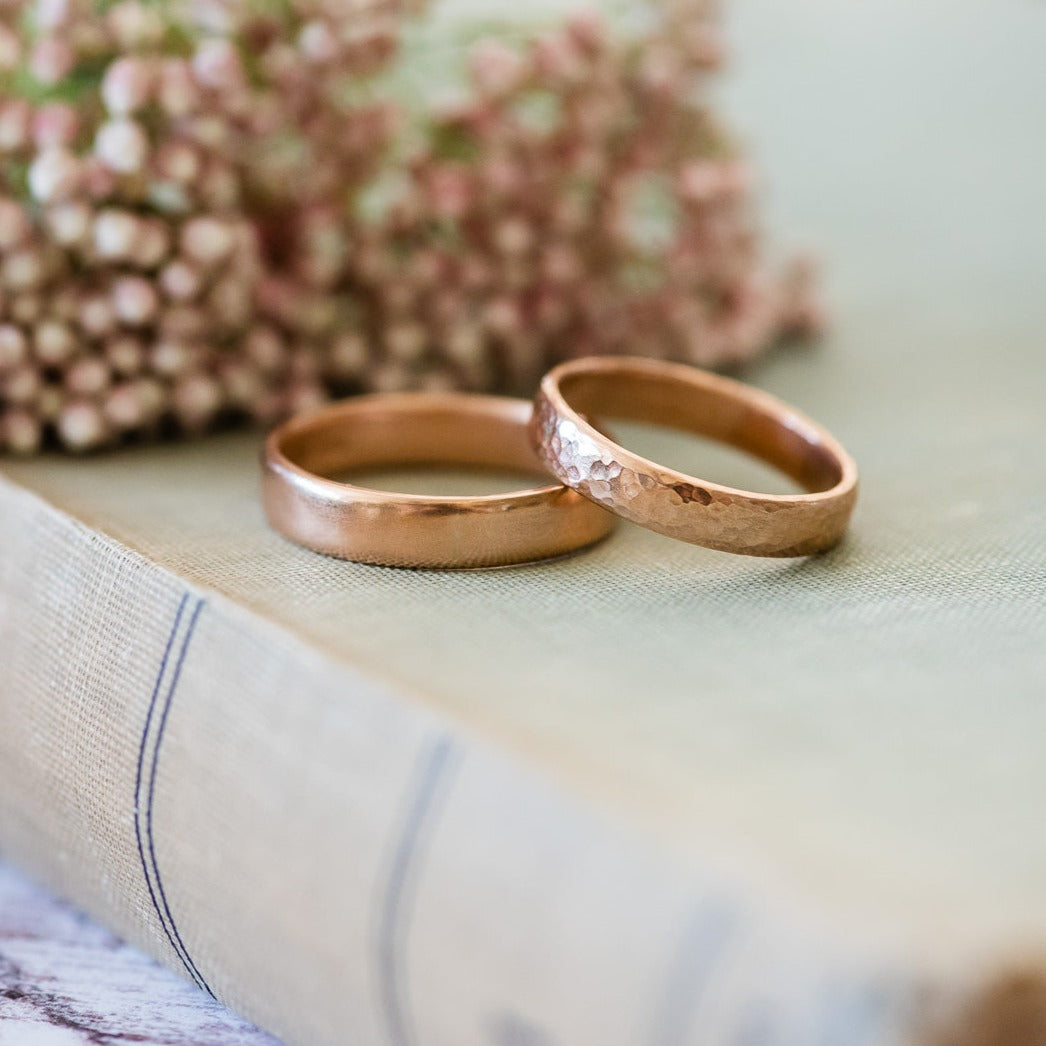 Two 9cr rose gold wedding bands sitting on book, with flowers in the background.