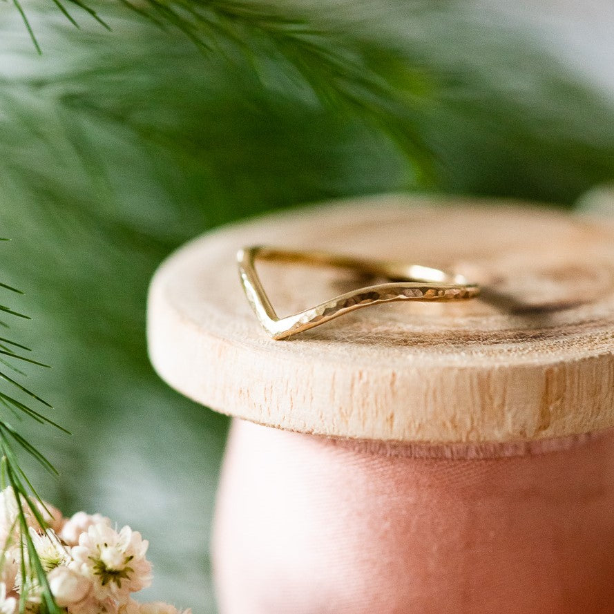 hammered wishbone wedding ring sitting on a wooden bobbin