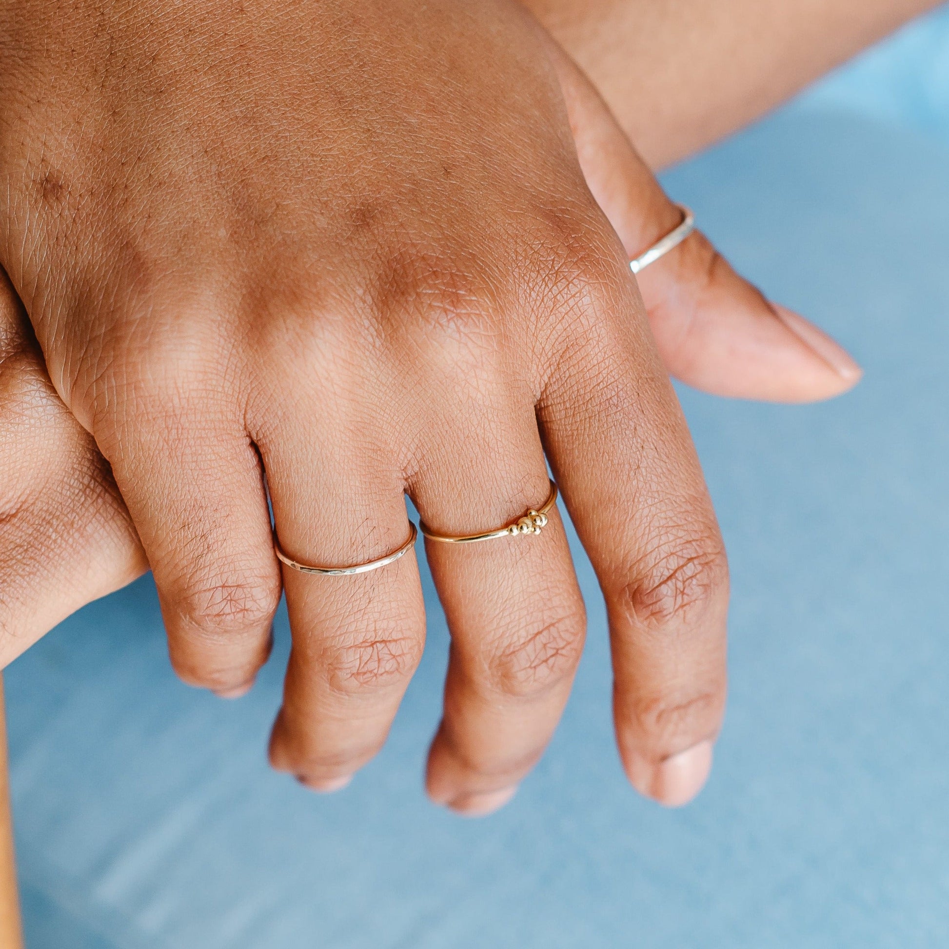 A hand wearing a pair of slim rings, one white gold with a hammered pattern, one gold with bubbles. 