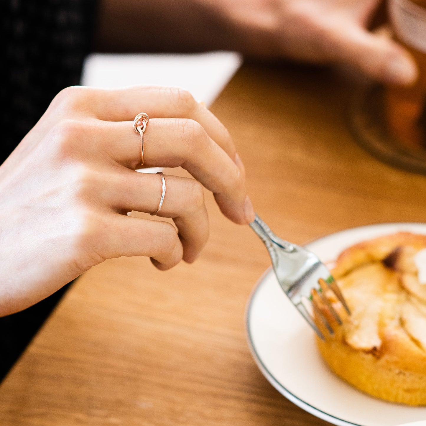 A silver twist ring and 9ct rose gold knot ring being worn. The hand is holding a fork over a cake