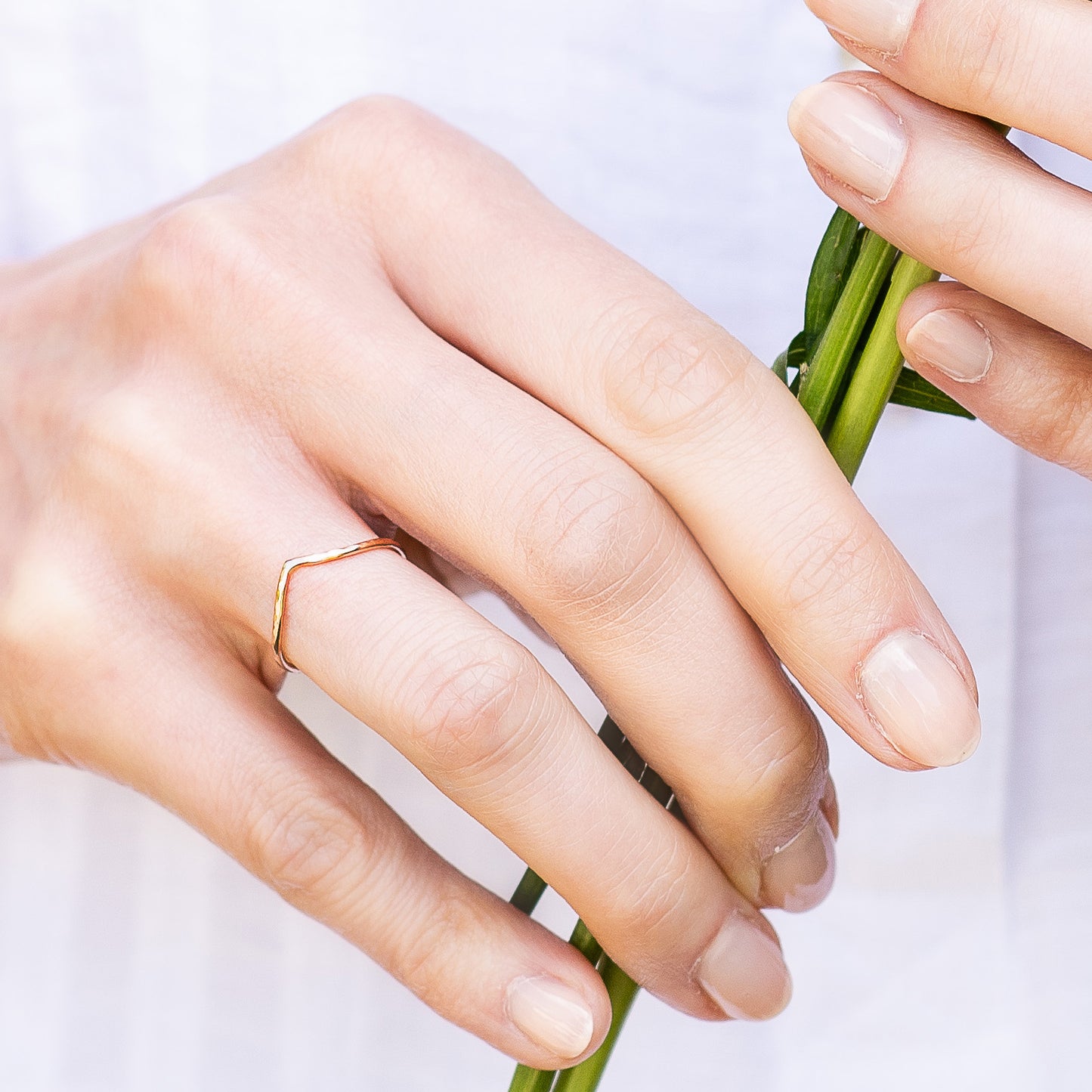 Thin wishbone ring 9ct rose gold, being worn, hand holding a flower stem
