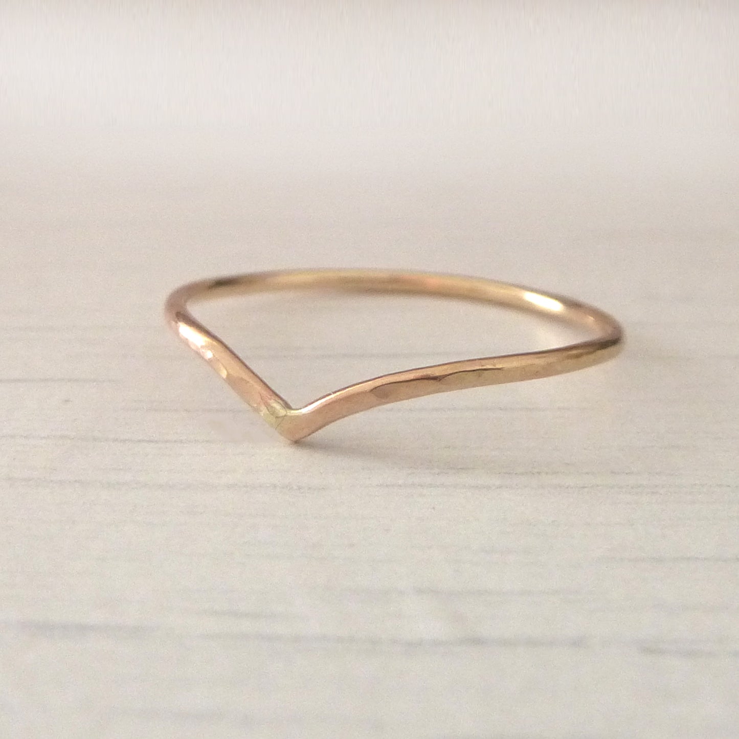 Thin wishbone ring in 9ct rose gold, sitting on wood background