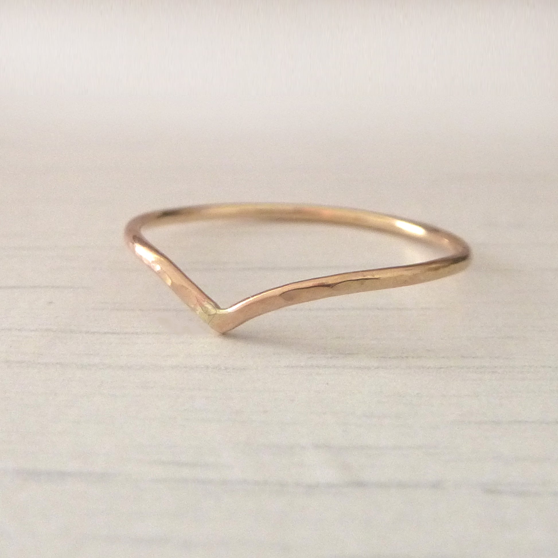 Thin wishbone ring in 9ct rose gold, sitting on wood background